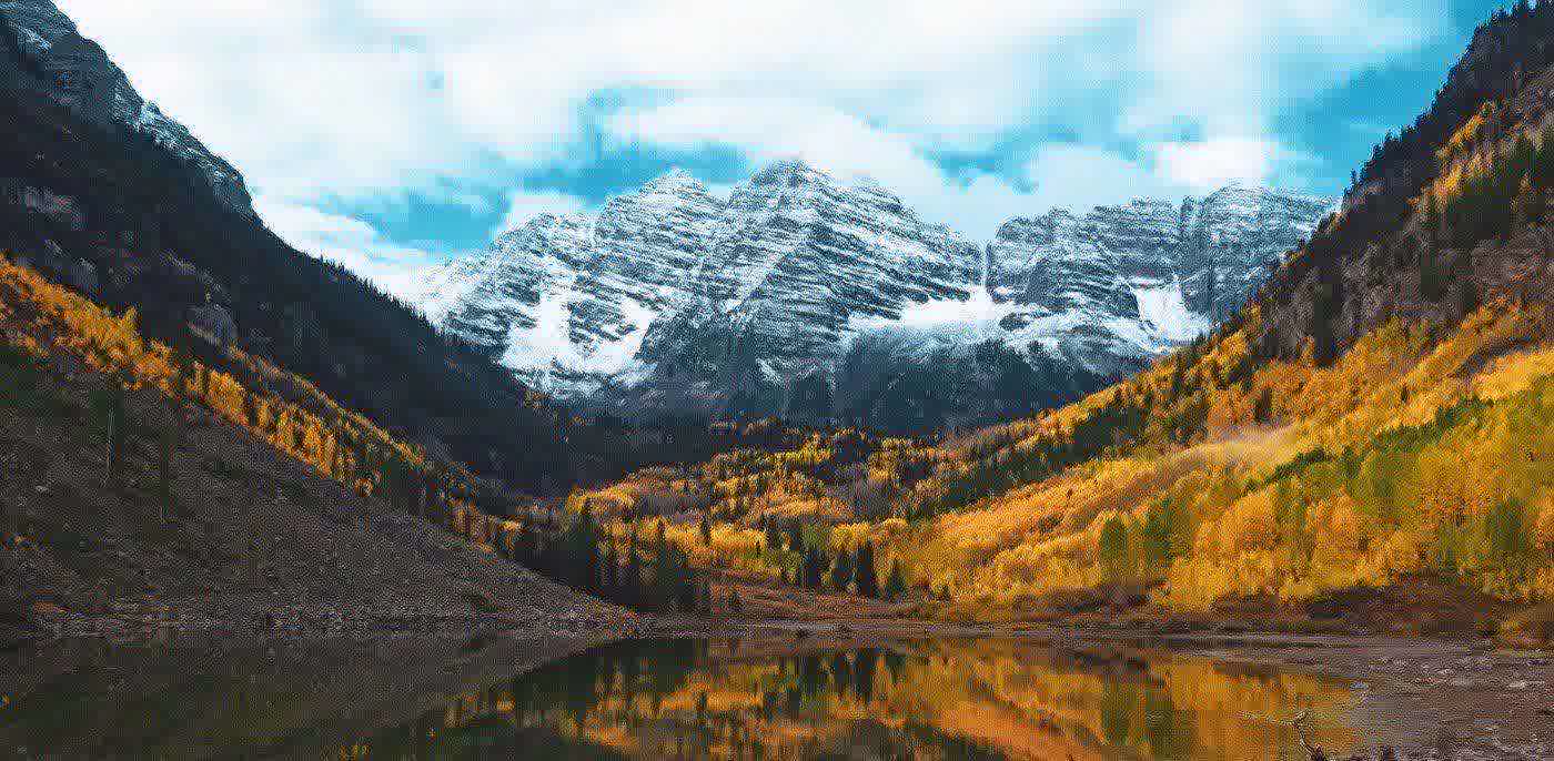 Snow-dusted Maroon Bells above golden aspen groves and an alpine lake